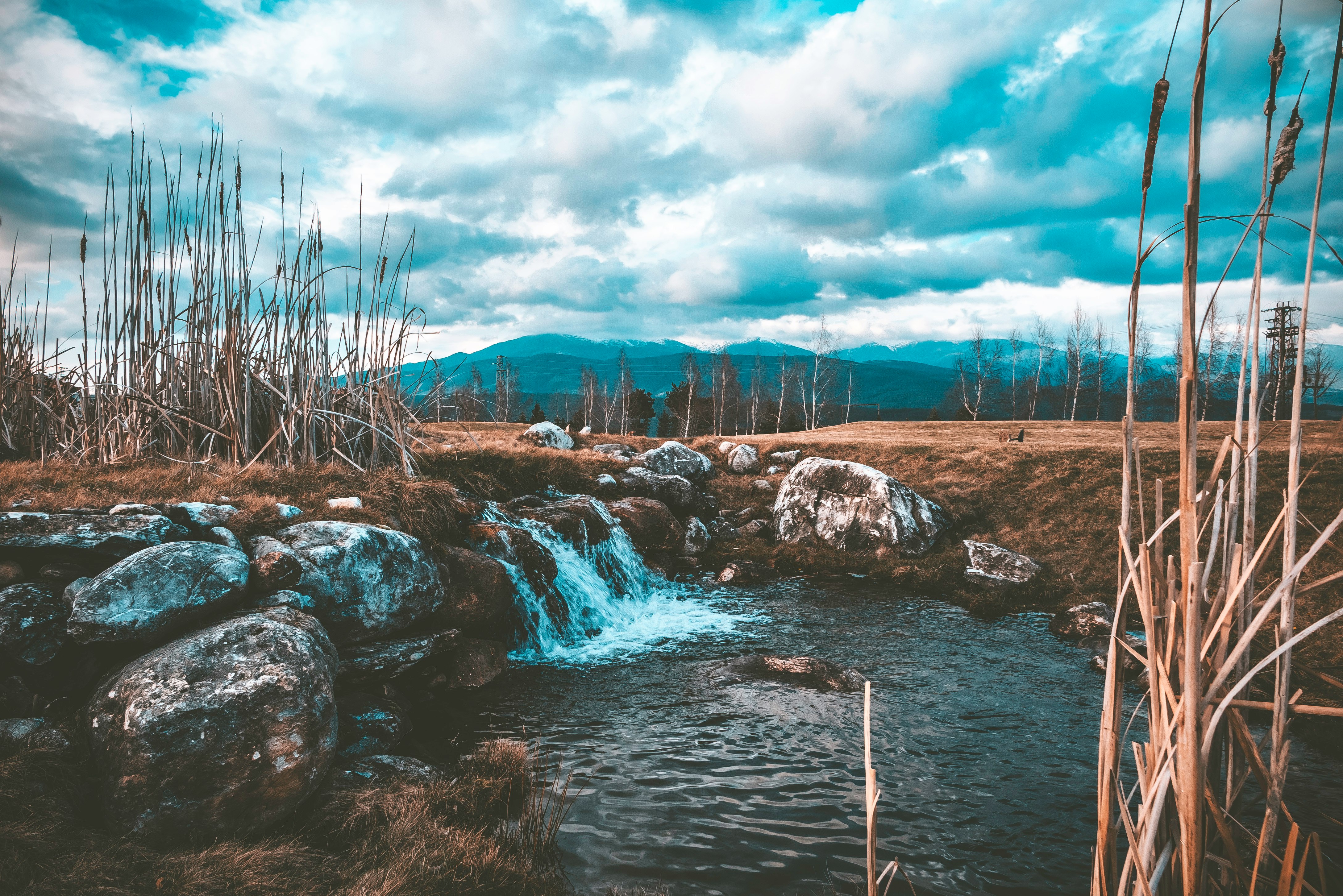 stream of water near brown soil and stone